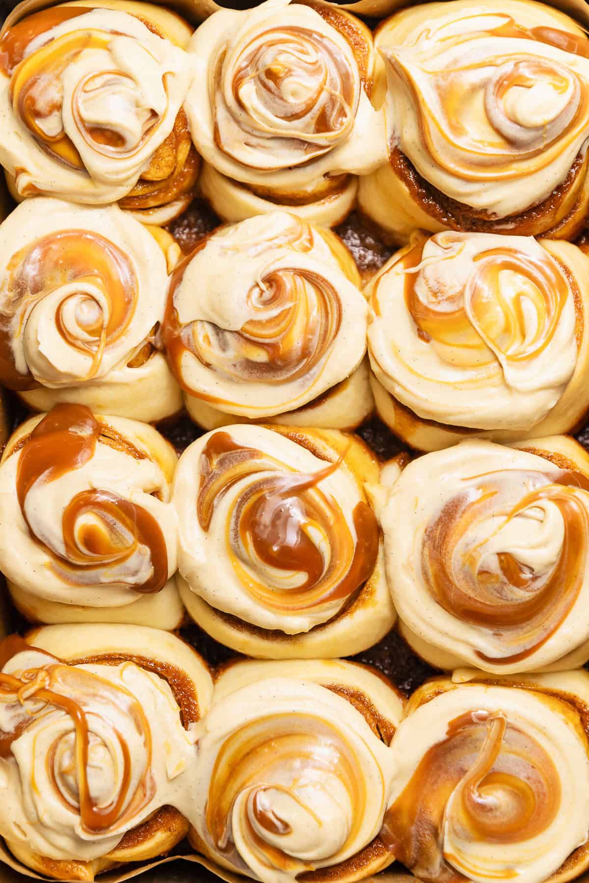 Overhead view of caramel cinnamon rolls topped with cream cheese frosting and salted caramel before it melts into the tops.
