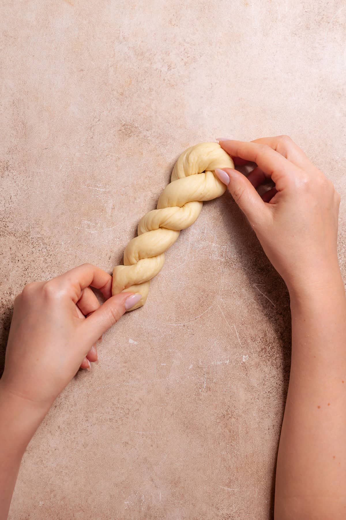 Hands pinching the ends of twisted donut dough together to finish shaping the donut.