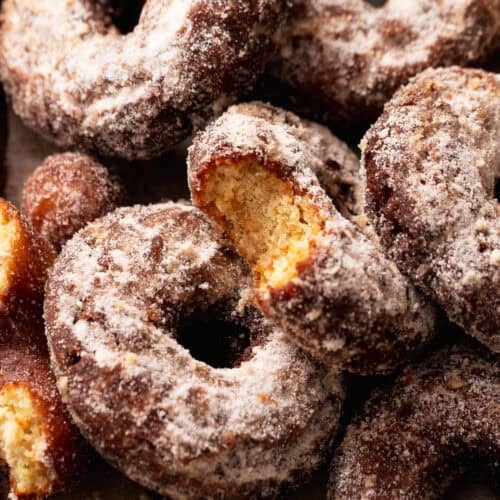 Close-up of apple cider cake donuts coated in cinnamon sugar, with one broken open to show the tender crumb.