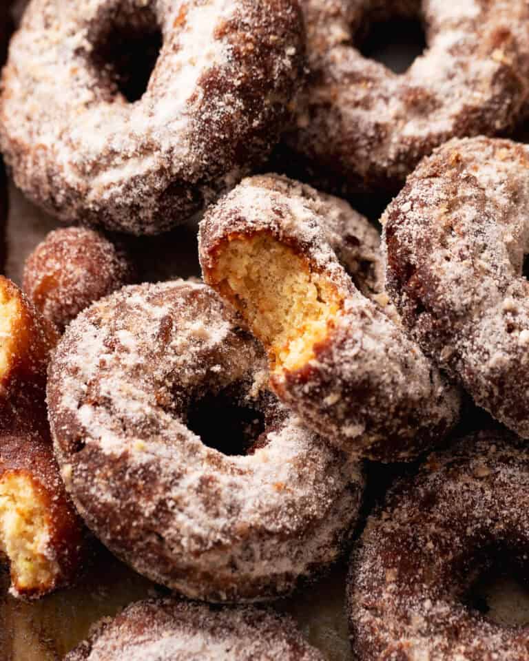 Close-up of apple cider cake donuts coated in cinnamon sugar, with one broken open to show the tender crumb.