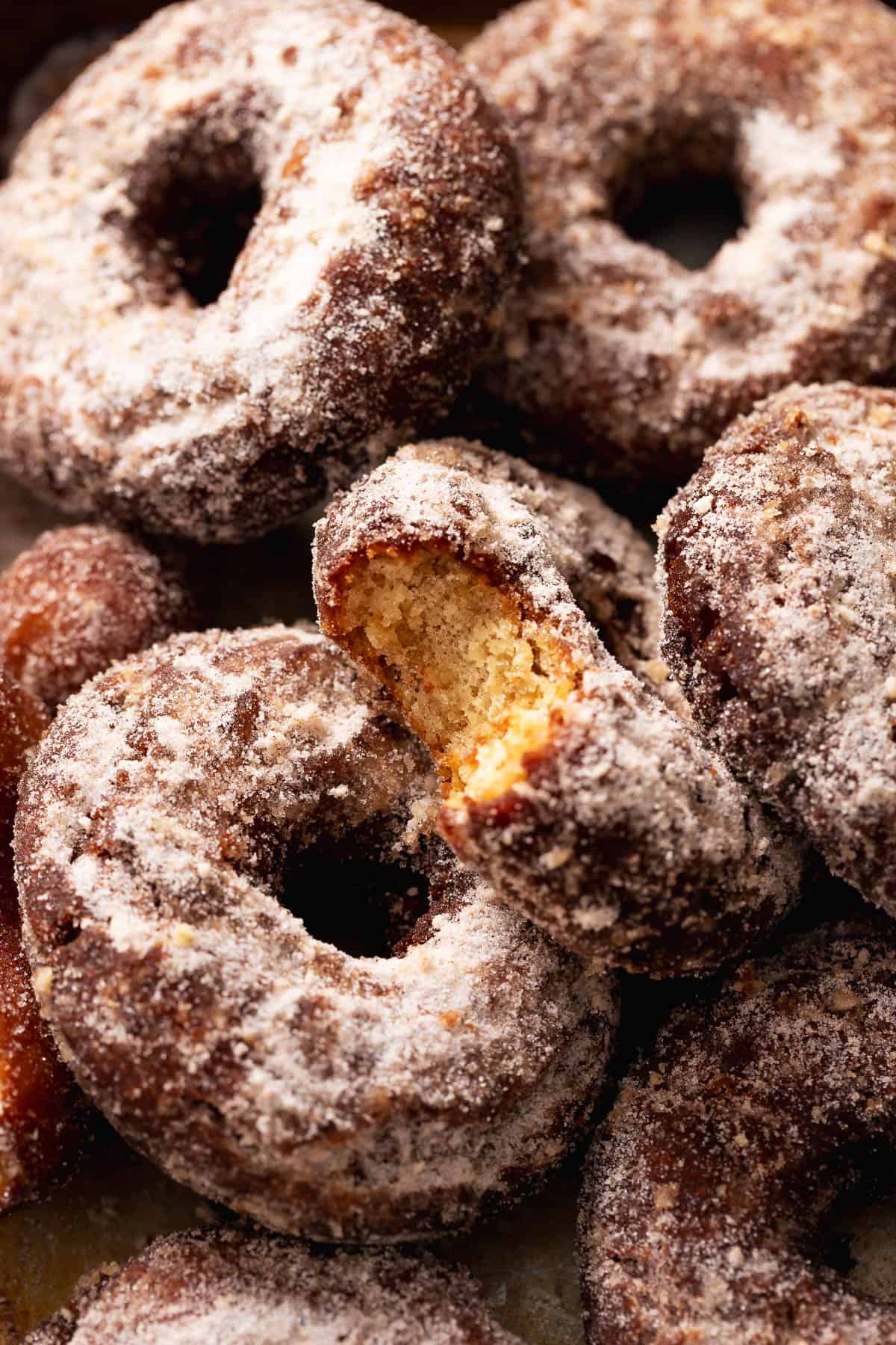 Cinnamon sugar apple cider donuts with a broken donut showing the soft, cakey interior.