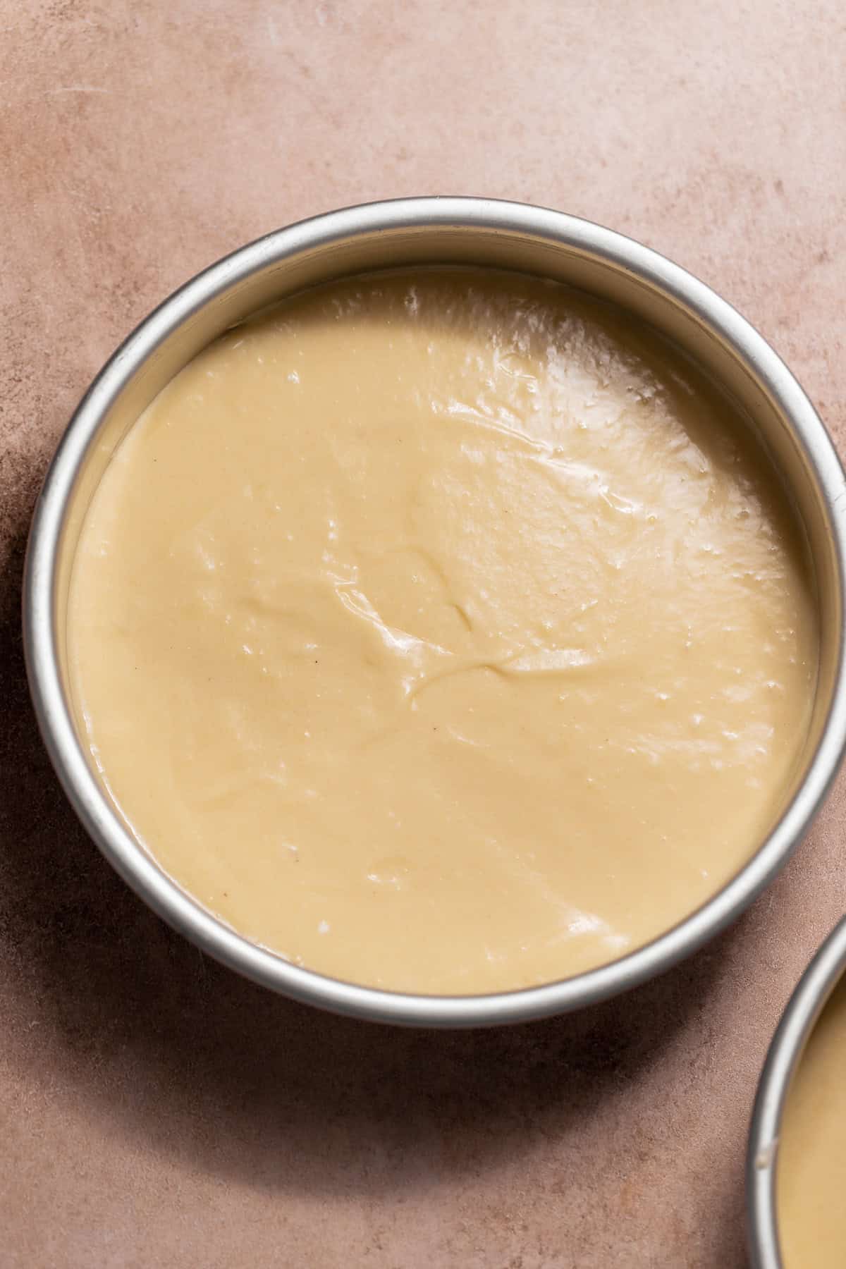 Overhead view of smooth, pale yellow vanilla cake batter spread evenly in a round metal cake pan.