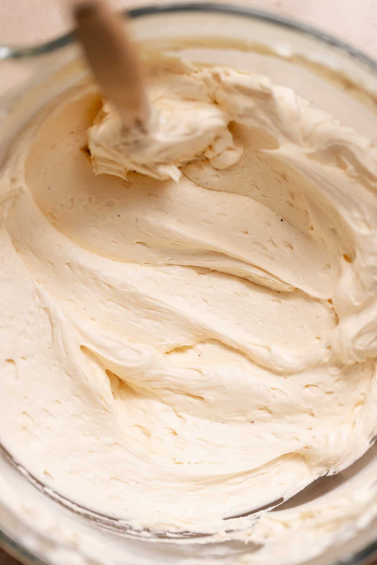 Close-up of thick, fluffy caramel buttercream frosting being mixed in a glass bowl, with soft swirls and air pockets.