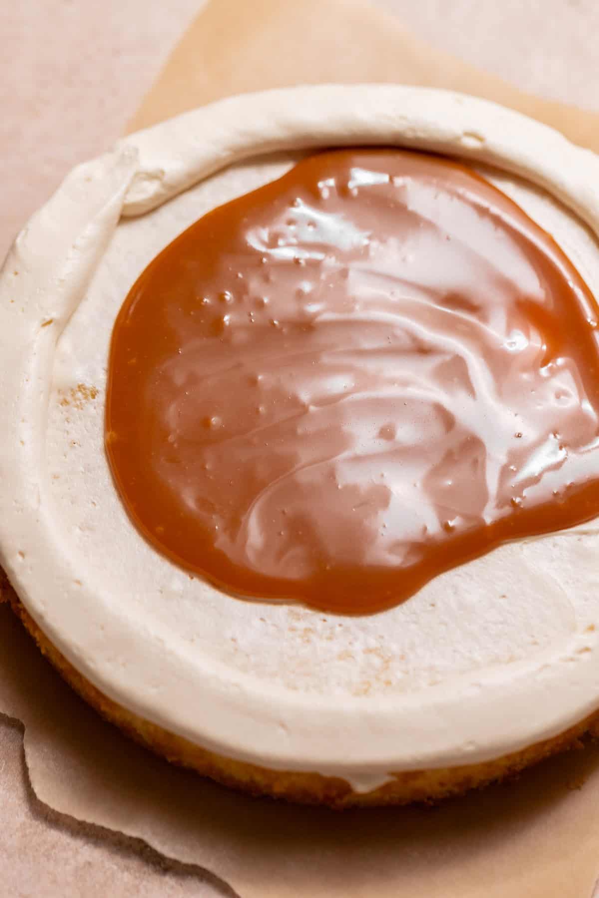 Overhead close-up of a vanilla cake layer with a thick ring of buttercream surrounding a pool of glossy caramel filling.