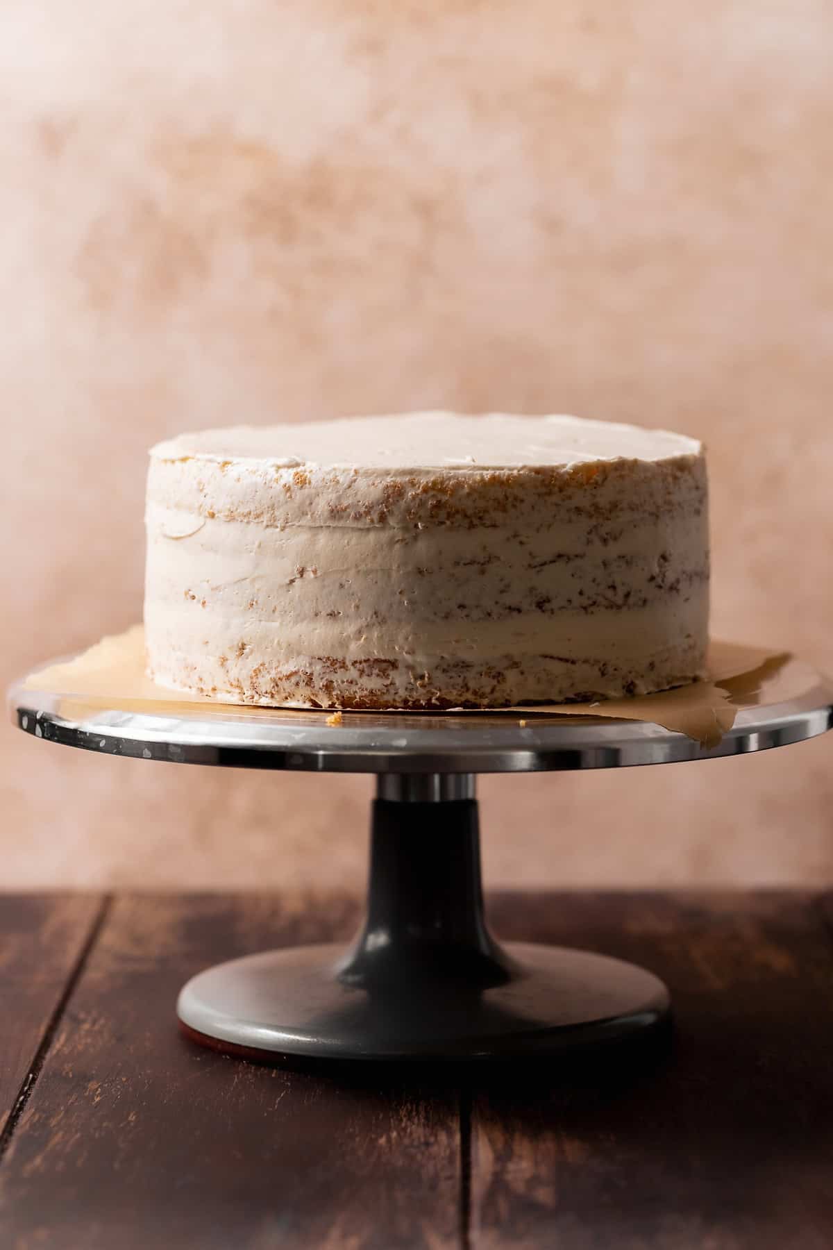 Three-layer cake covered in a thin, semi-transparent coat of buttercream frosting on a rotating metal cake stand.