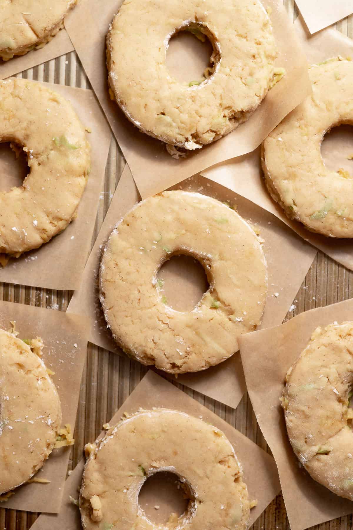 Cut apple cider donut dough rounds resting on individual squares of parchment paper before frying.