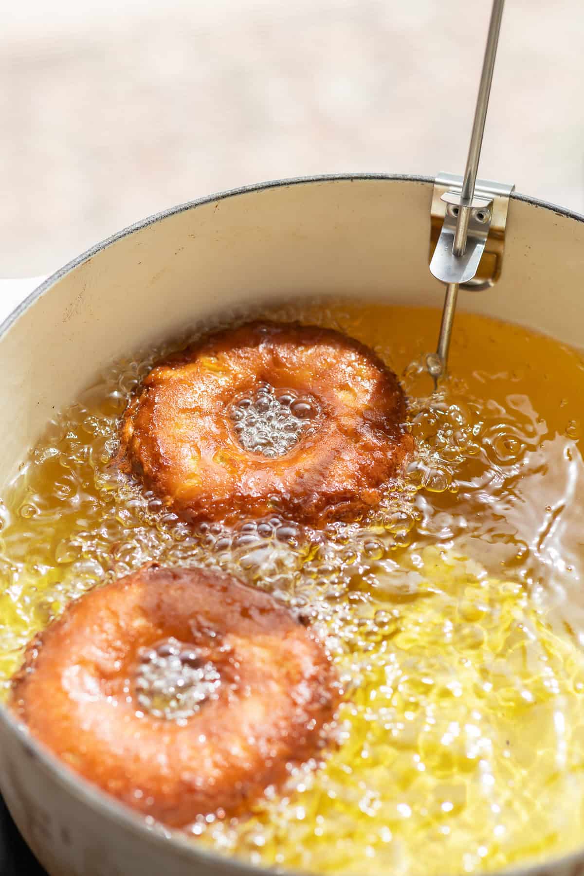 Apple cider donuts frying in hot oil with a thermometer clipped to the side of the pot.