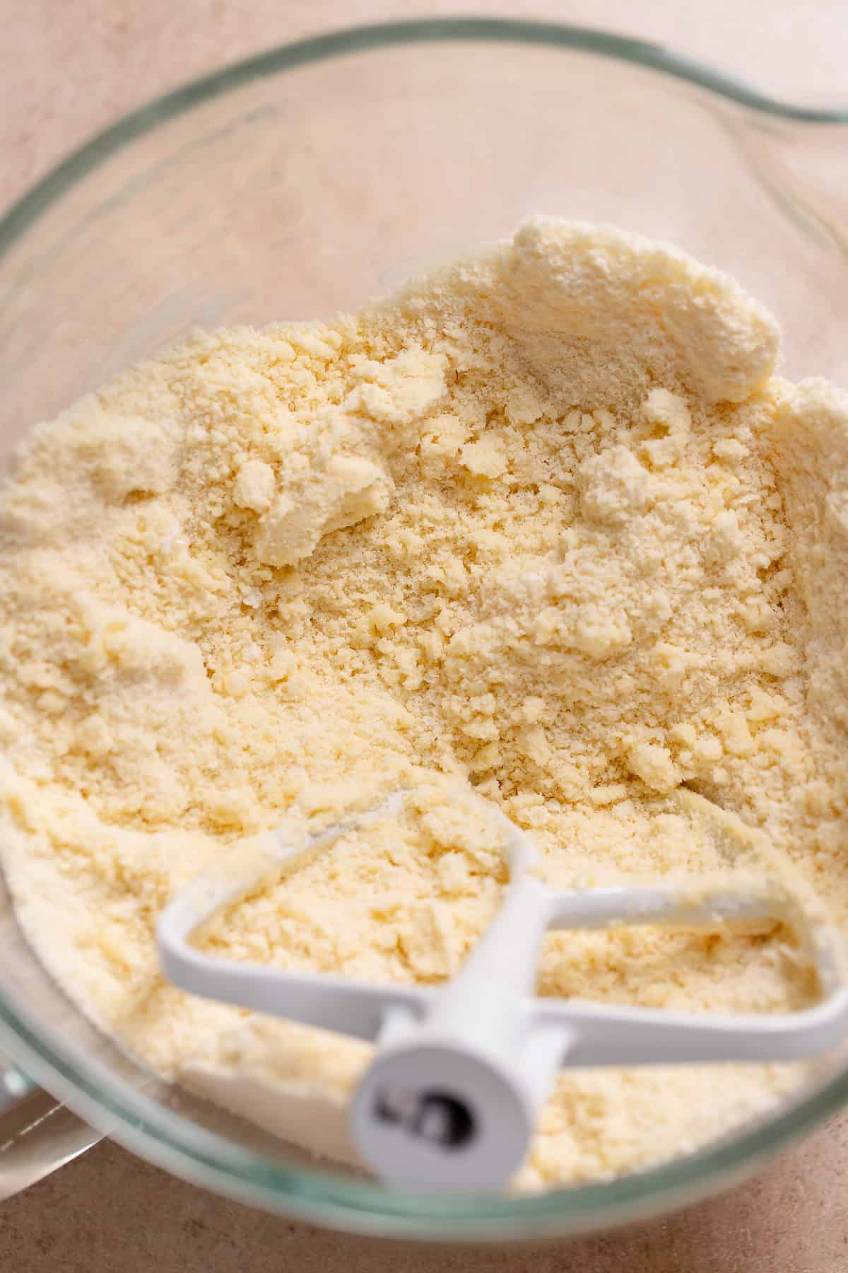 Reverse-creamed cake batter with a crumbly, sandy texture in a glass mixing bowl with a paddle attachment.
