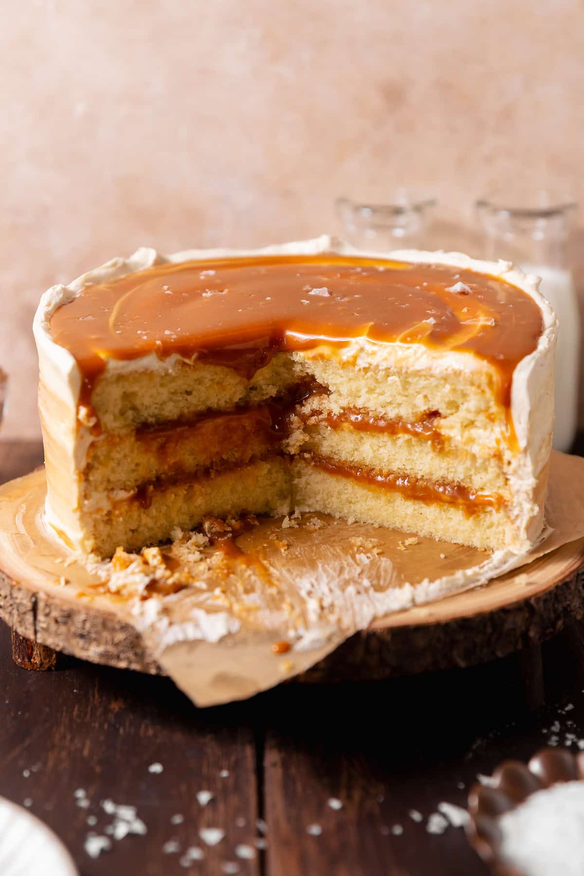 Salted caramel cake with a slice removed, revealing three layers of vanilla cake and gooey caramel filling, topped with glossy salted caramel.