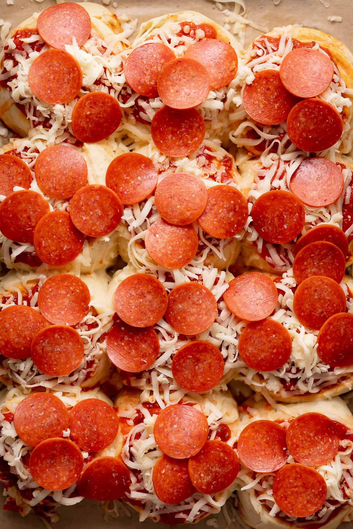 An overhead shot of the rolls half baked and topped with more cheese and mini pepperonis.