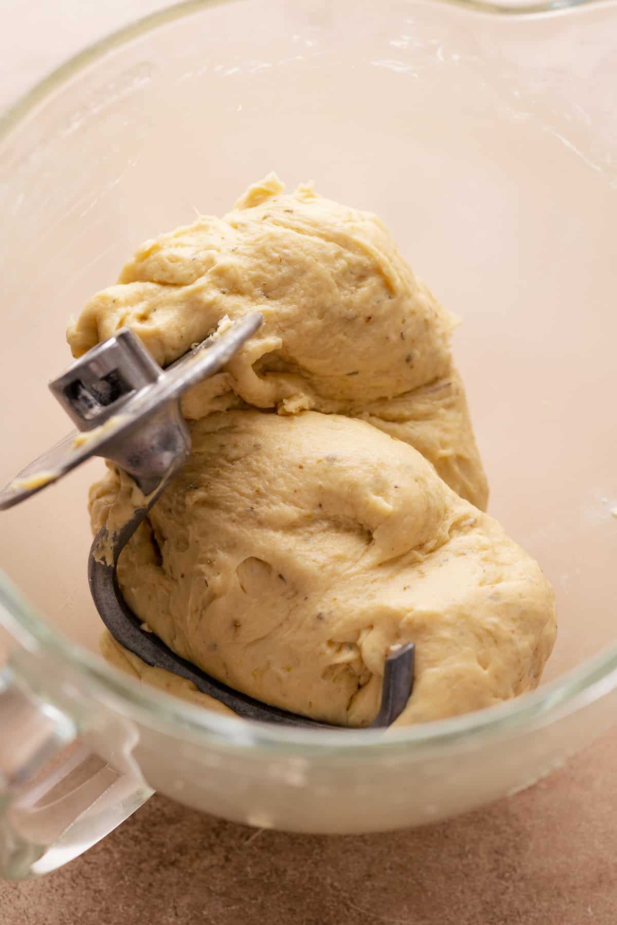 Dough being kneaded by a metal dough hook in a glass mixing bowl.