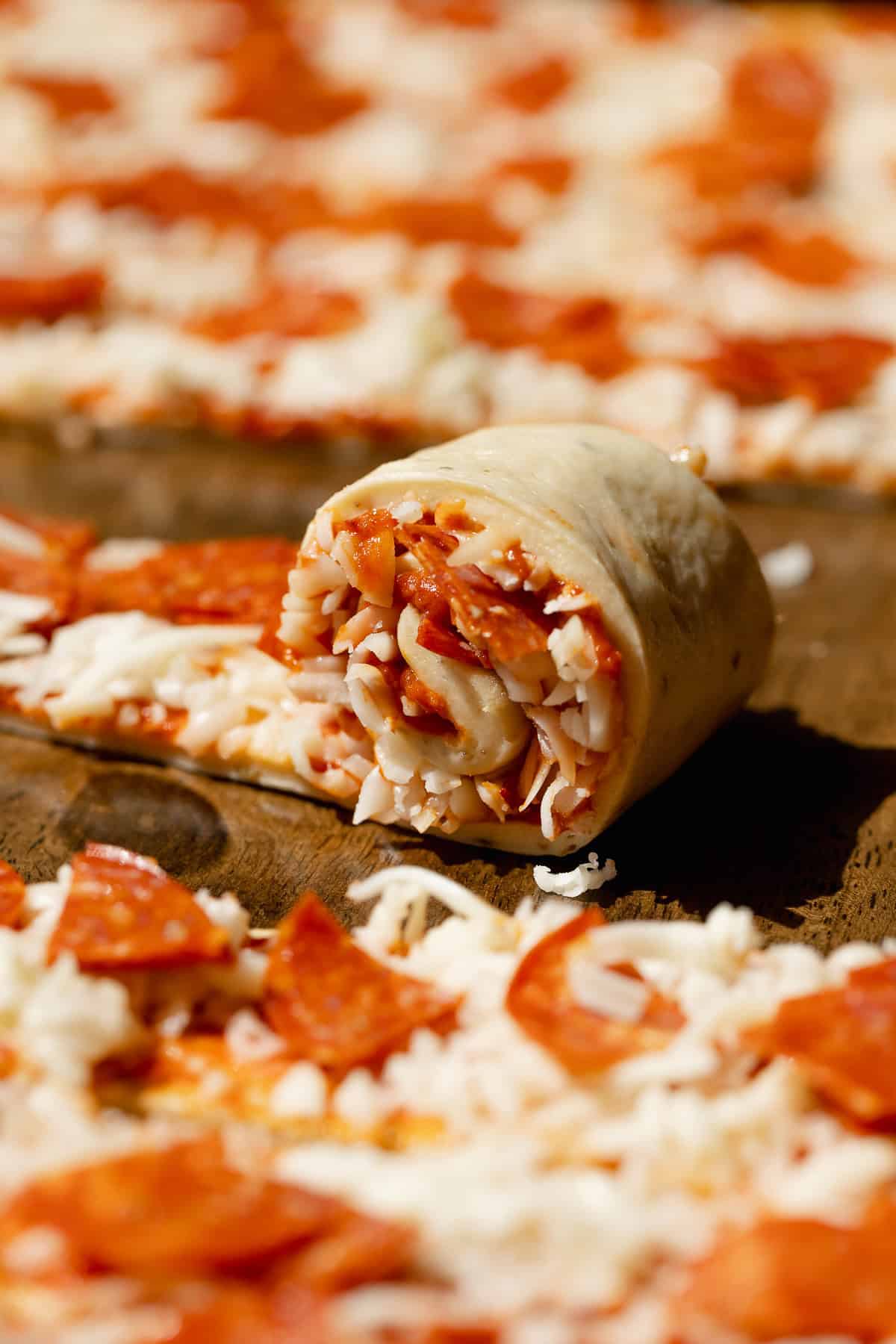 A strip of homemade pizza dough rolled into a spiral with pepperoni slices, shredded mozzarella cheese, and tomato pizza sauce inside.