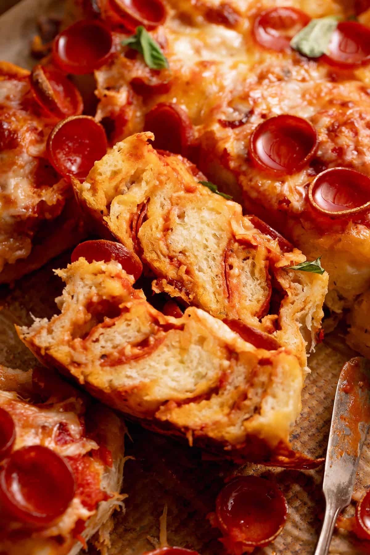 A close-up of a pepperoni pizza bread roll, cut in half with melted cheese and fresh basil.