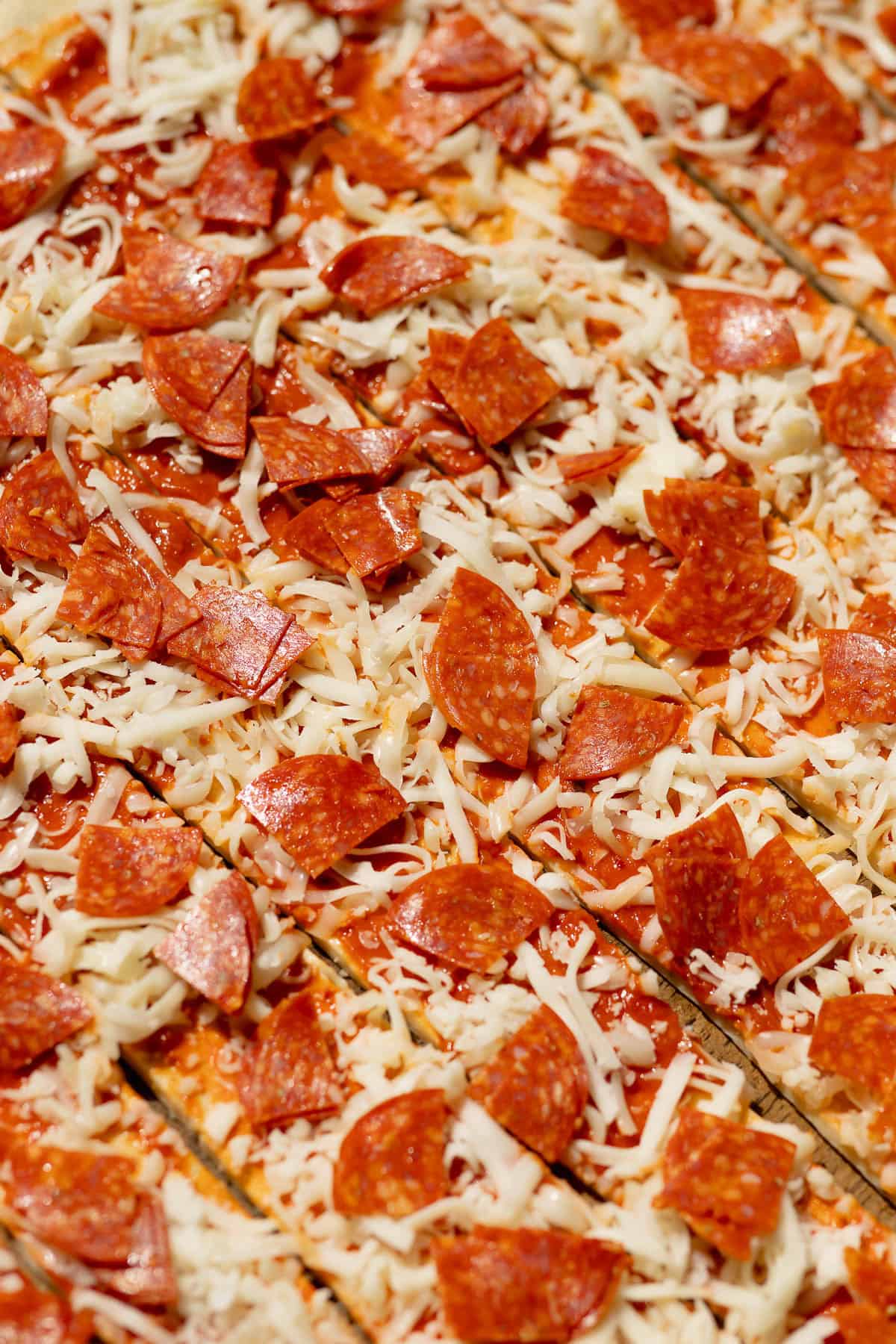 Quartered pepperoni slices scattered over shredded mozzarella cheese and pizza sauce on strips of homemade dough before rolling.