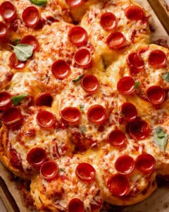 Pull-apart pepperoni pizza rolls topped with melted cheese and fresh basil leaves.