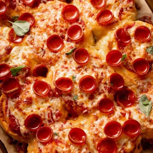 Pull-apart pepperoni pizza rolls topped with melted cheese and fresh basil leaves.