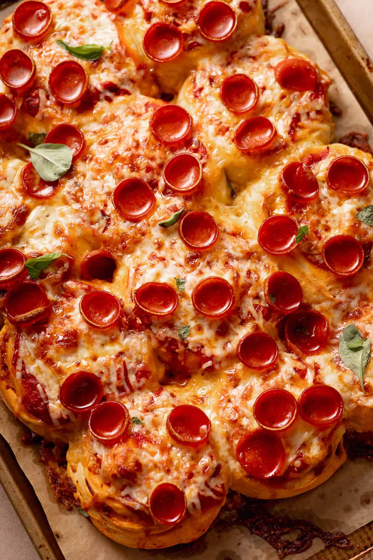 Pull-apart pepperoni pizza rolls topped with melted cheese and fresh basil leaves on a baking sheet.