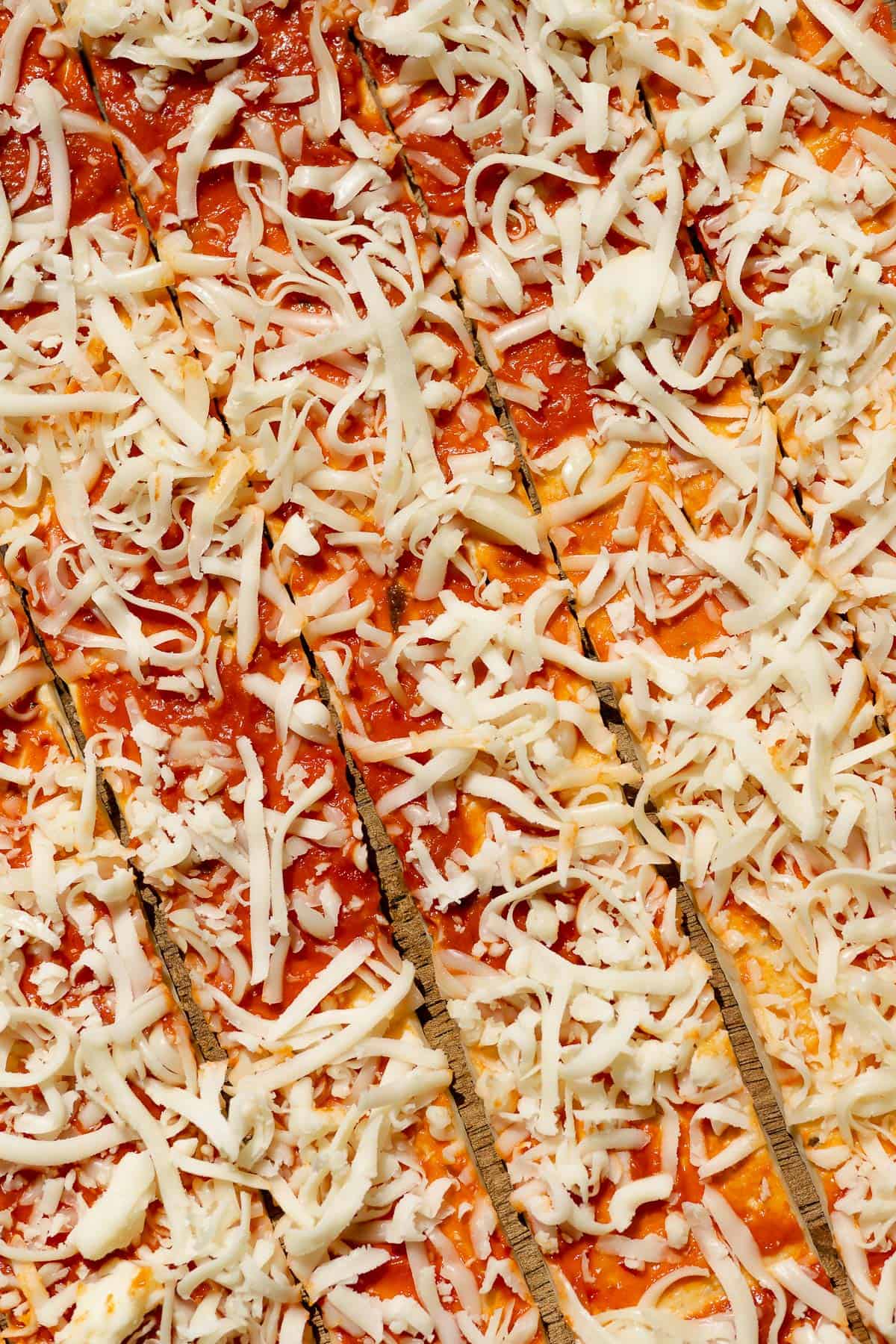 Strips of dough topped with tomato sauce and shredded mozzarella cheese.
